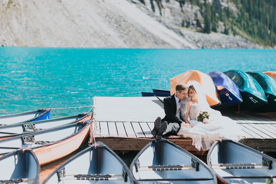 Moraine Lake bride & groom portraits with turquoise blue water, mountains & colorful canoes
