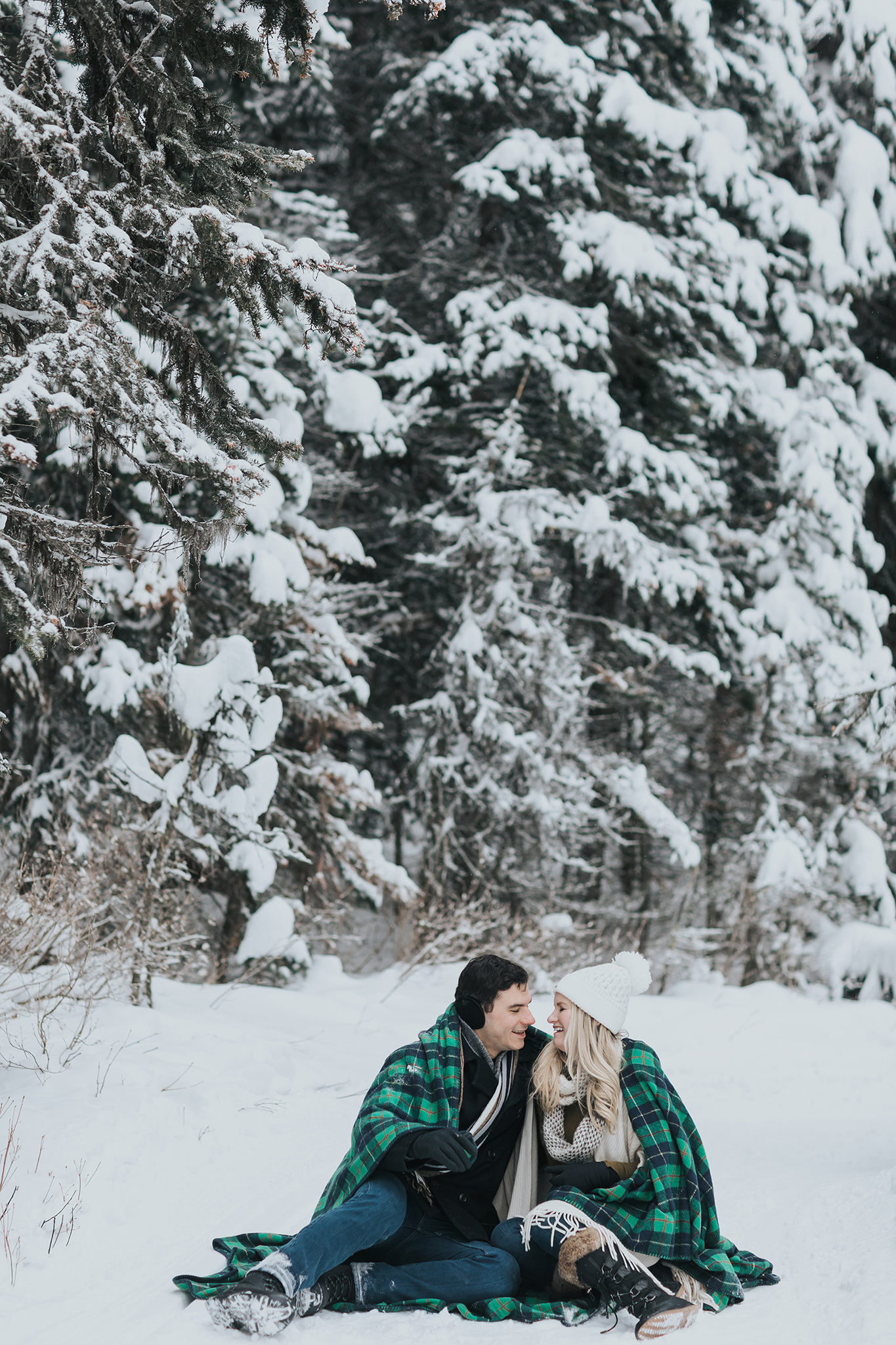cuddly couples session in the snow during winter. Woodland forest couples pictures green plaid blanket