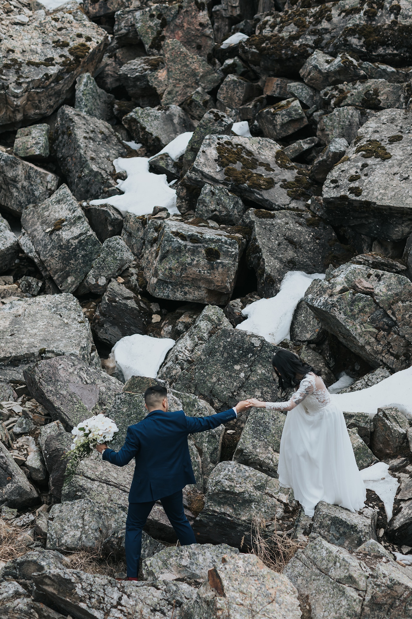 mountain wedding in late spring. Bride & groom climbing the Rock Pile at Moraine Lake