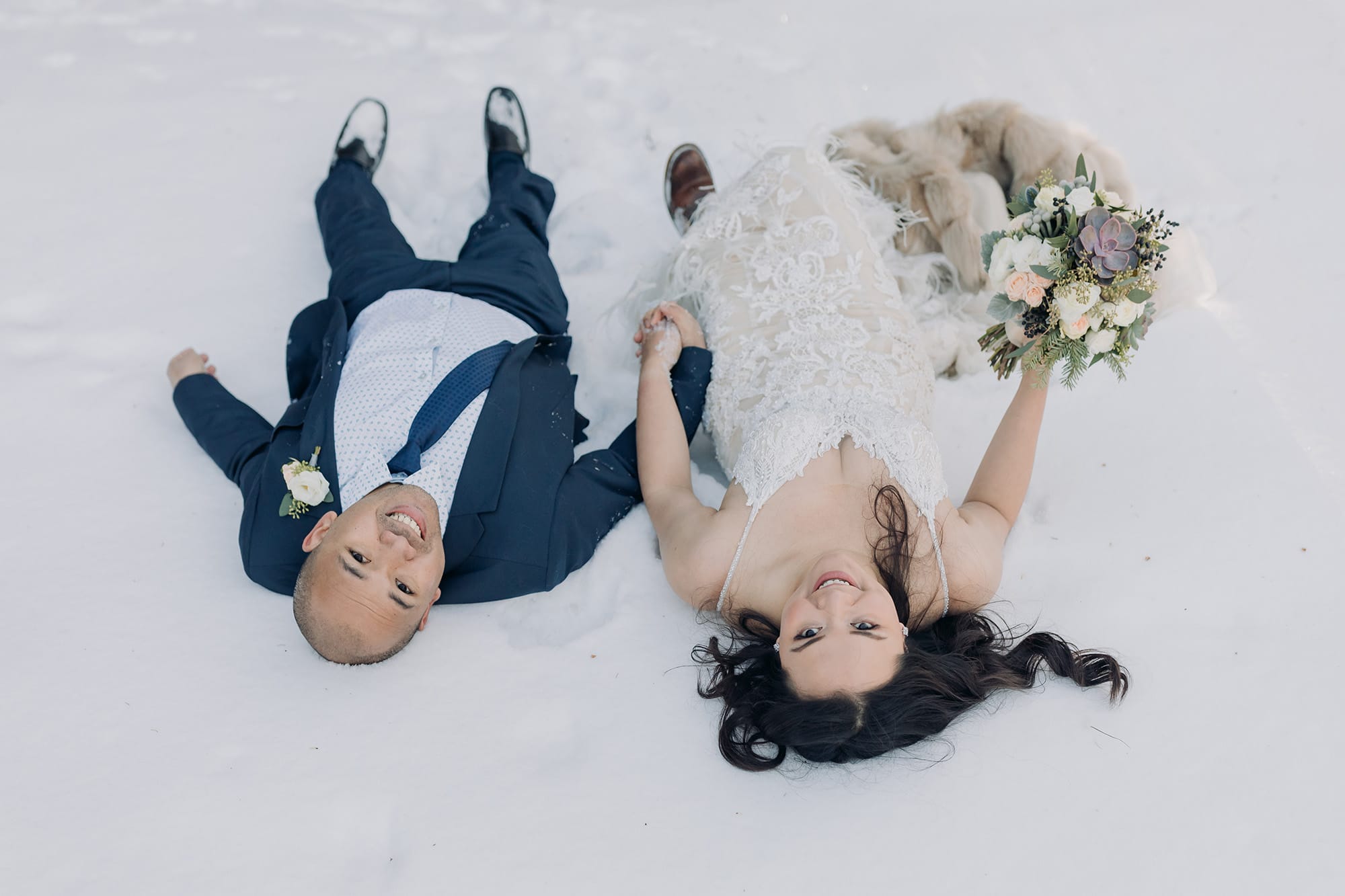 bride & groom laying in the snow on their wedding day