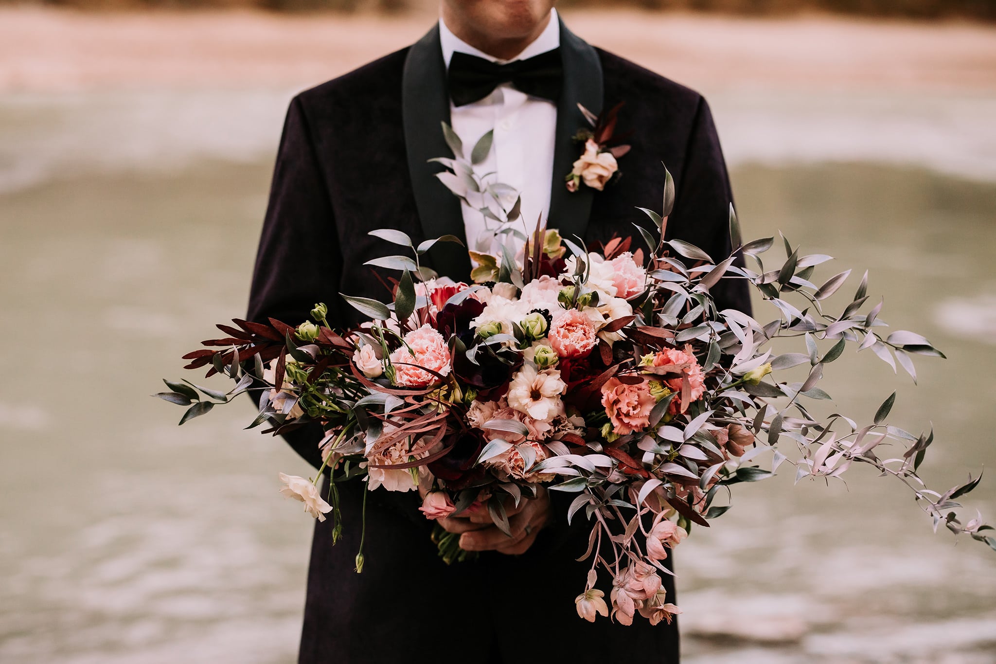 groom holding dark moody wedding bouquet