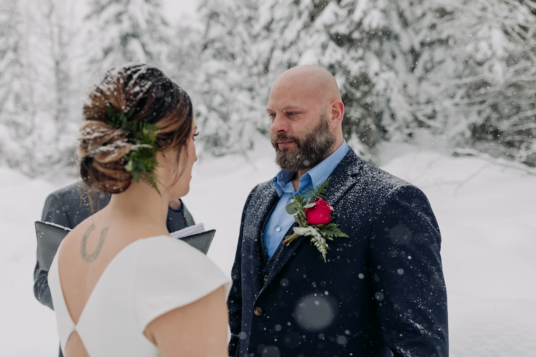 Emerald Lake Lodge winter elopement outdoor wedding ceremony in the pathway amongst the cabin with a natural tree arch with falling snow photographed by mountain elopement & wedding photographer ENV Photography