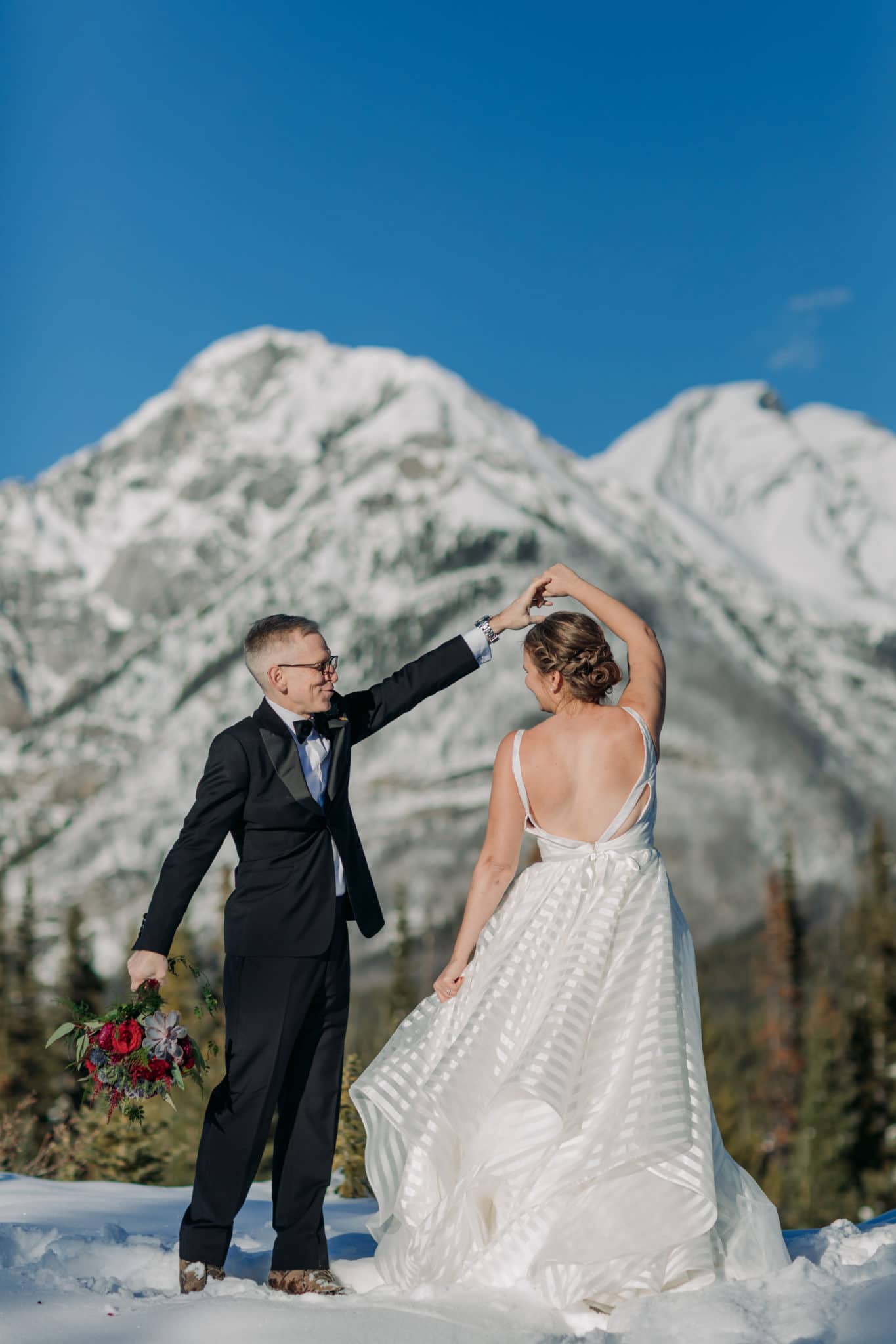 A Guide to Eloping in the Canadian Rockies | Mountain Wedding photographed by ENV Photography | Groom twirling bride in striped Hayley Paige gown in Kanananaskis near Mount Engadine Lodge