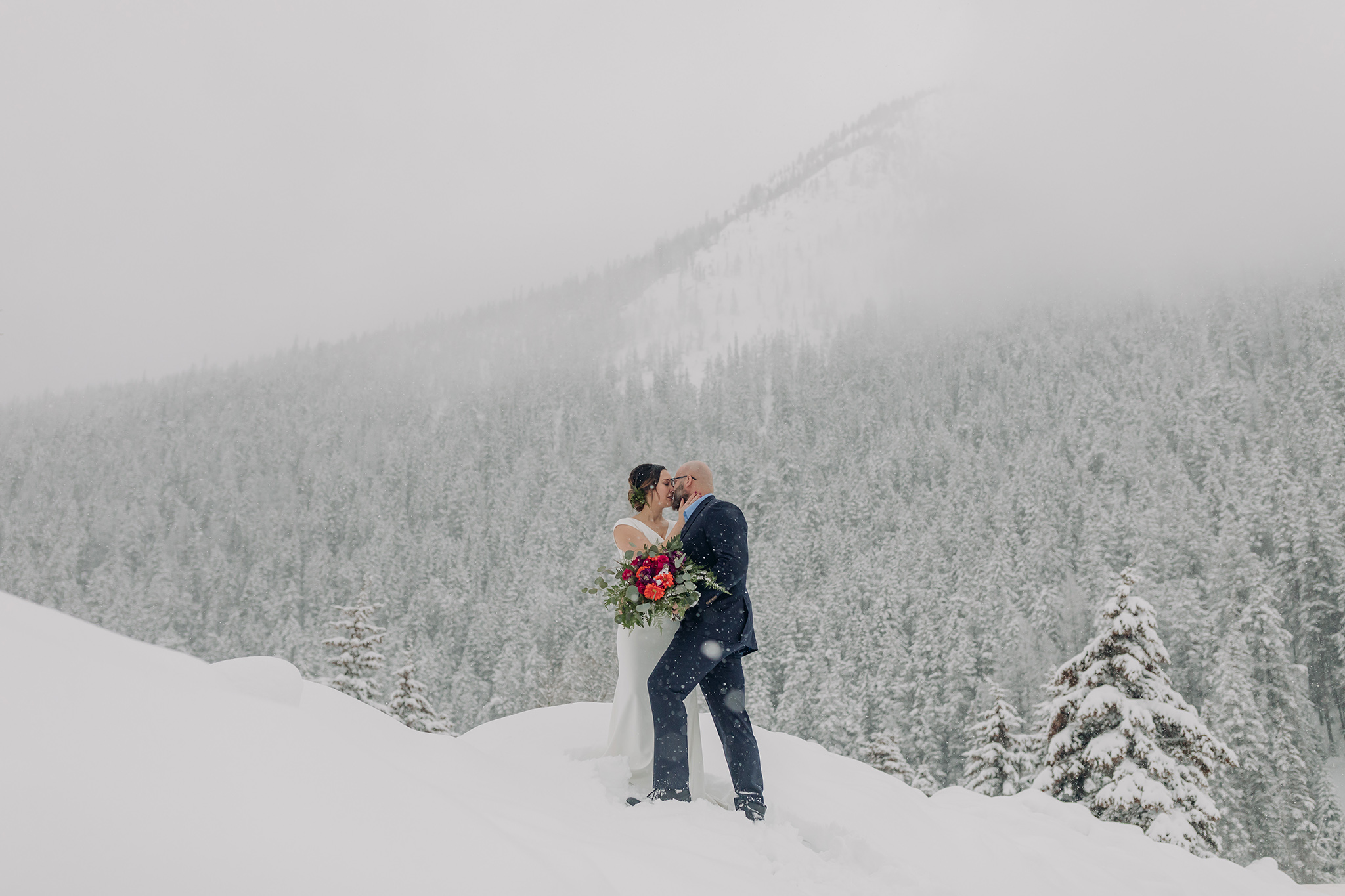 snowy mountain elopement bride & groom portraits climbing snow bank with falling snow photographed by mountain elopement & wedding photographer ENV Photography