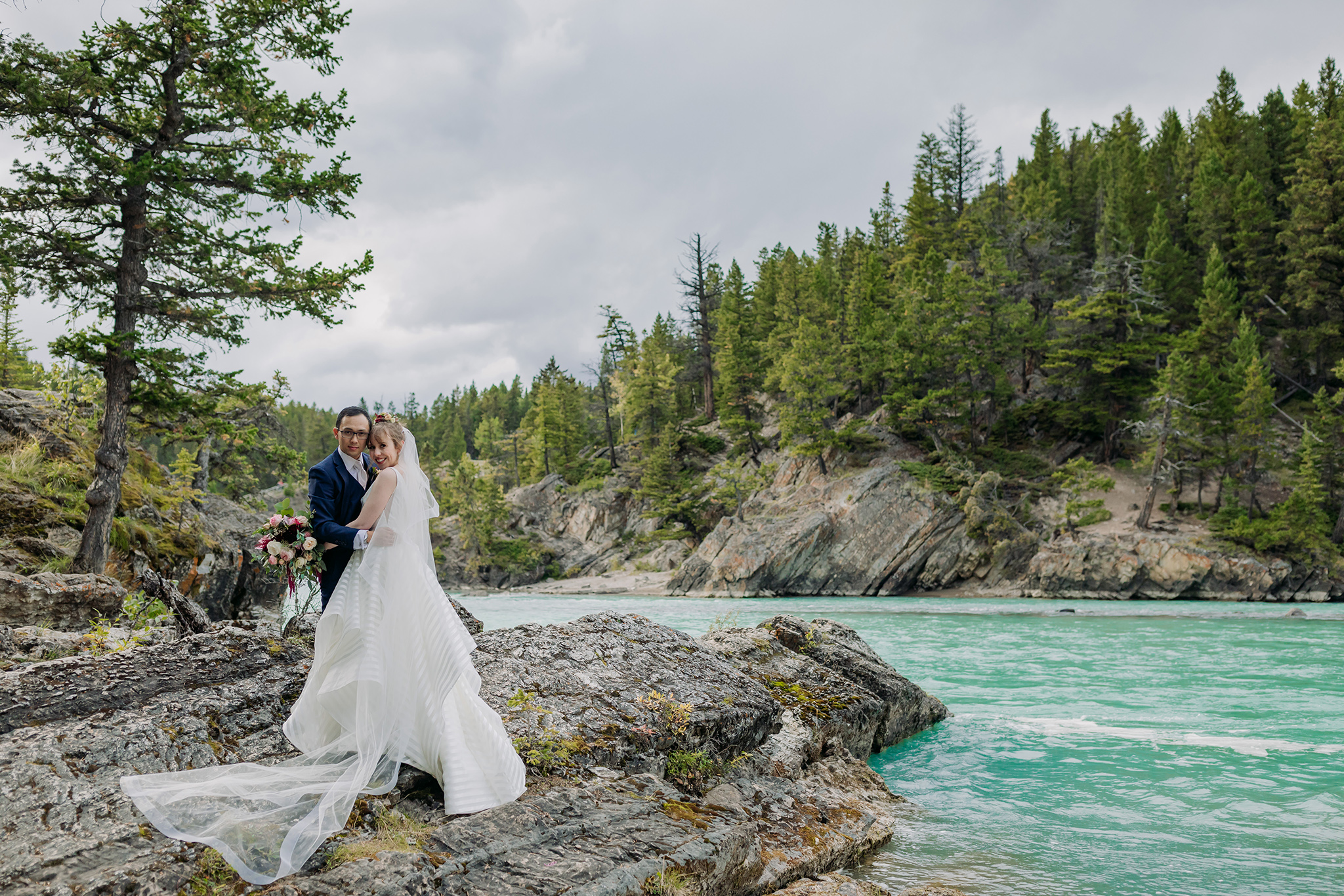 A Guide to Eloping in the Canadian Rockies | Mountain Wedding photographed by ENV Photography | Fairmont Banff Springs fall wedding with bride in striped Hayley Paige gown on the rocks near Bow Falls in Banff