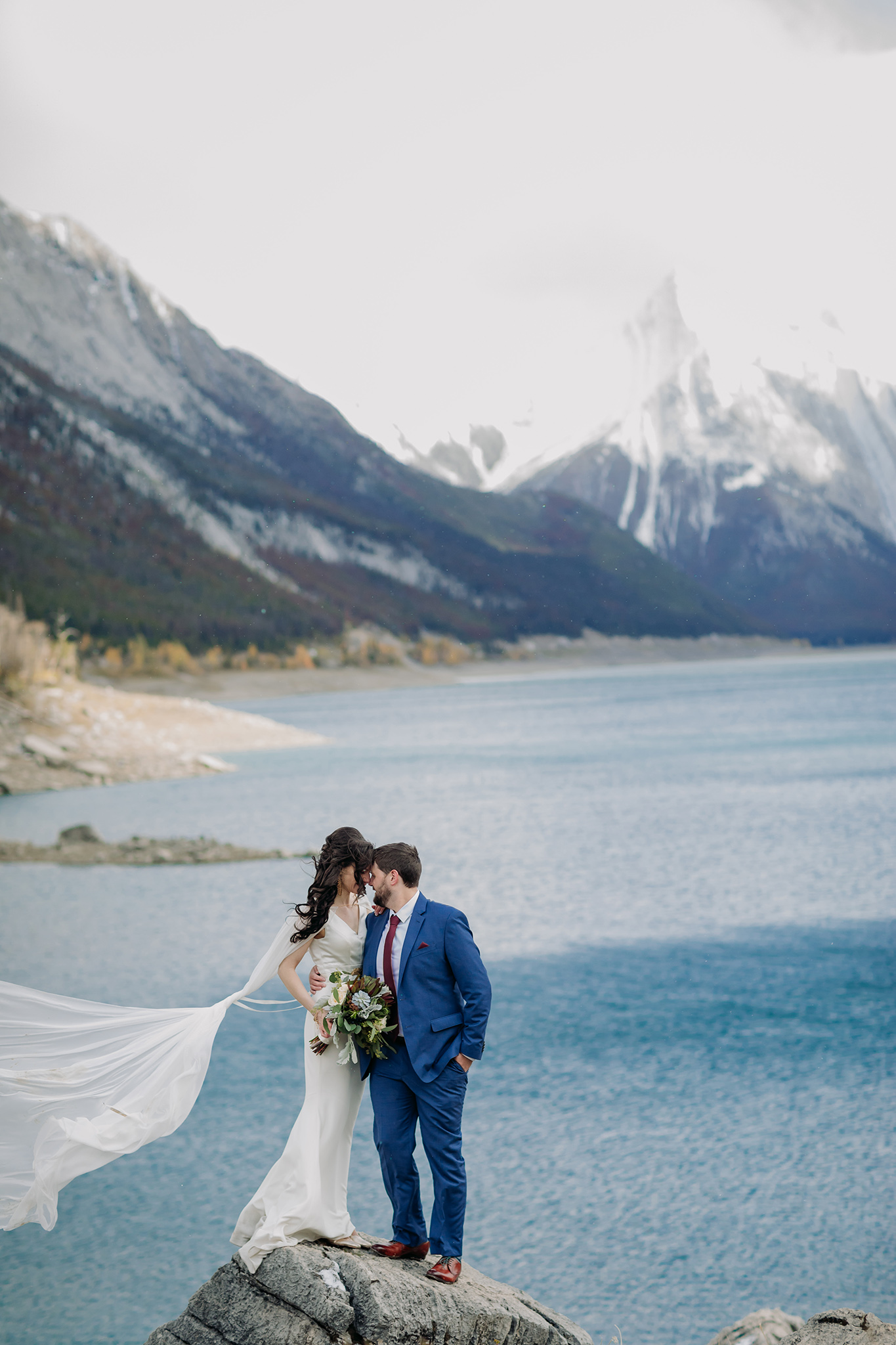 A Guide to Eloping in the Canadian Rockies | Mountain Wedding photographed by ENV Photography | windy autumn wedding at Medicine Lake in Jasper National Park. Bride wearing cape in the wind.
