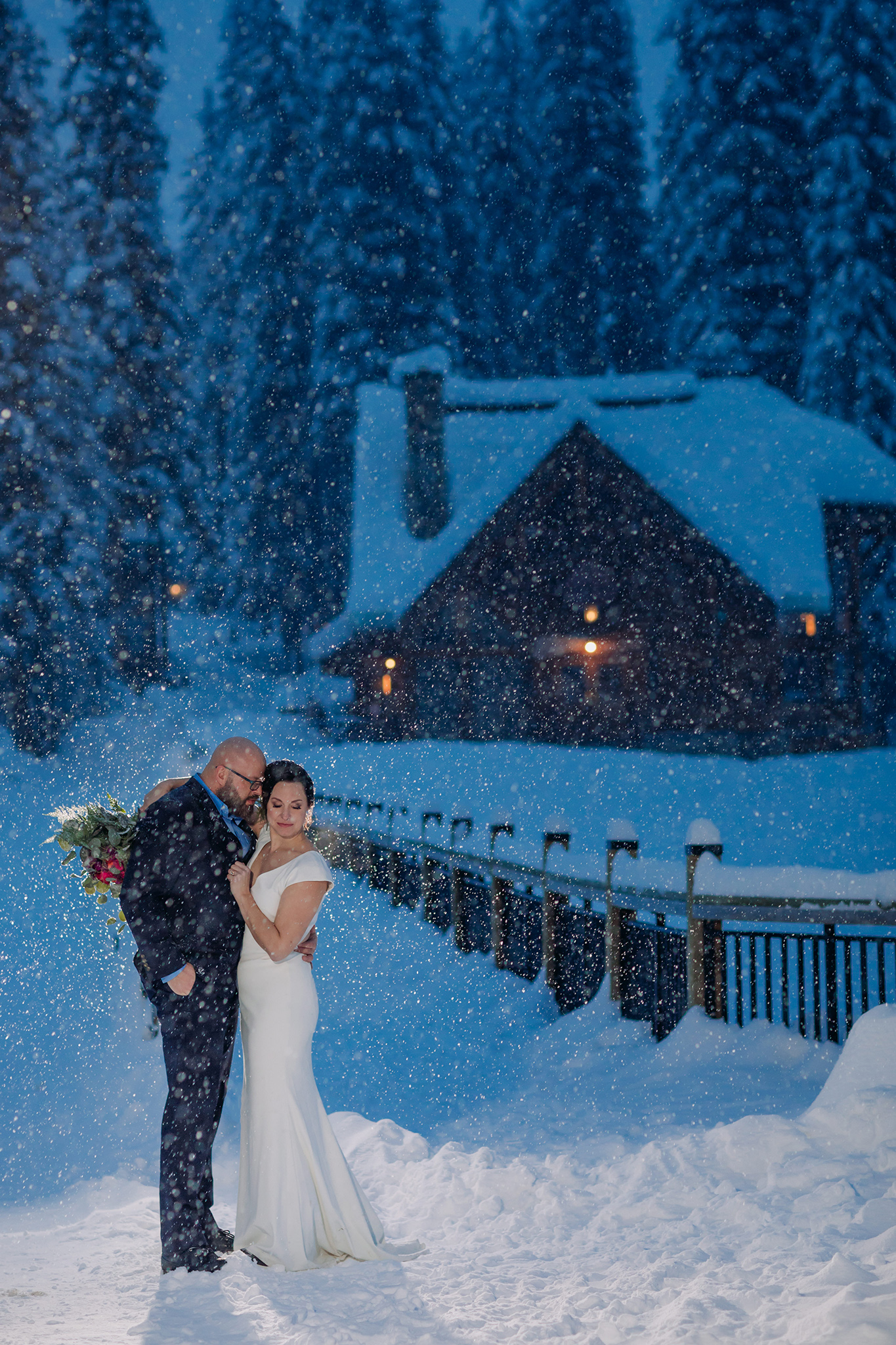 Emerald Lake Lodge winter elopement outdoor bride & groom portraits with backlit falling snow during twilight blue hour photographed by mountain elopement & wedding photographer ENV Photography