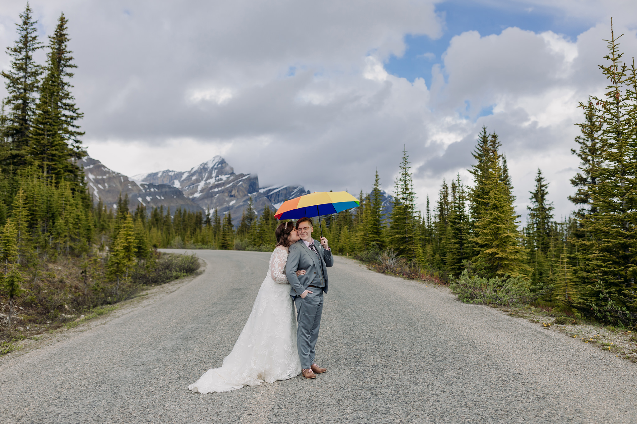 Icefields Parkway adventure session on road to Peyto Lake with same-sex wedding couple with rainbow umbrella days after their wedding. Mountain Wedding portraits photographed by ENV Photography. Gay friendly. LGBTQ friendly wedding & elopement photographer.