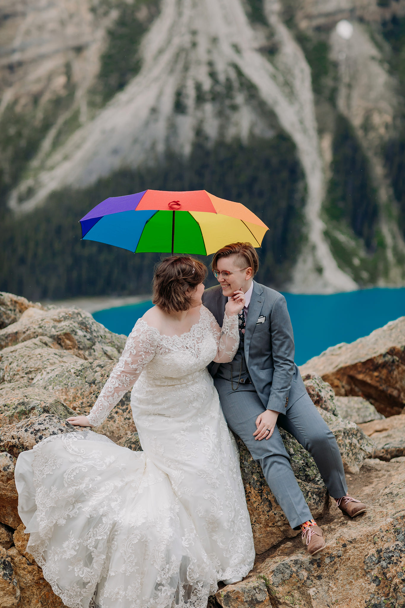 Wedding portraits with rainbow umbrella at rocky viewpoint at Peyto Lake. same-sex wedding. Mountain Wedding portraits photographed by ENV Photography. Gay friendly. LGBTQ friendly wedding & elopement photographer.