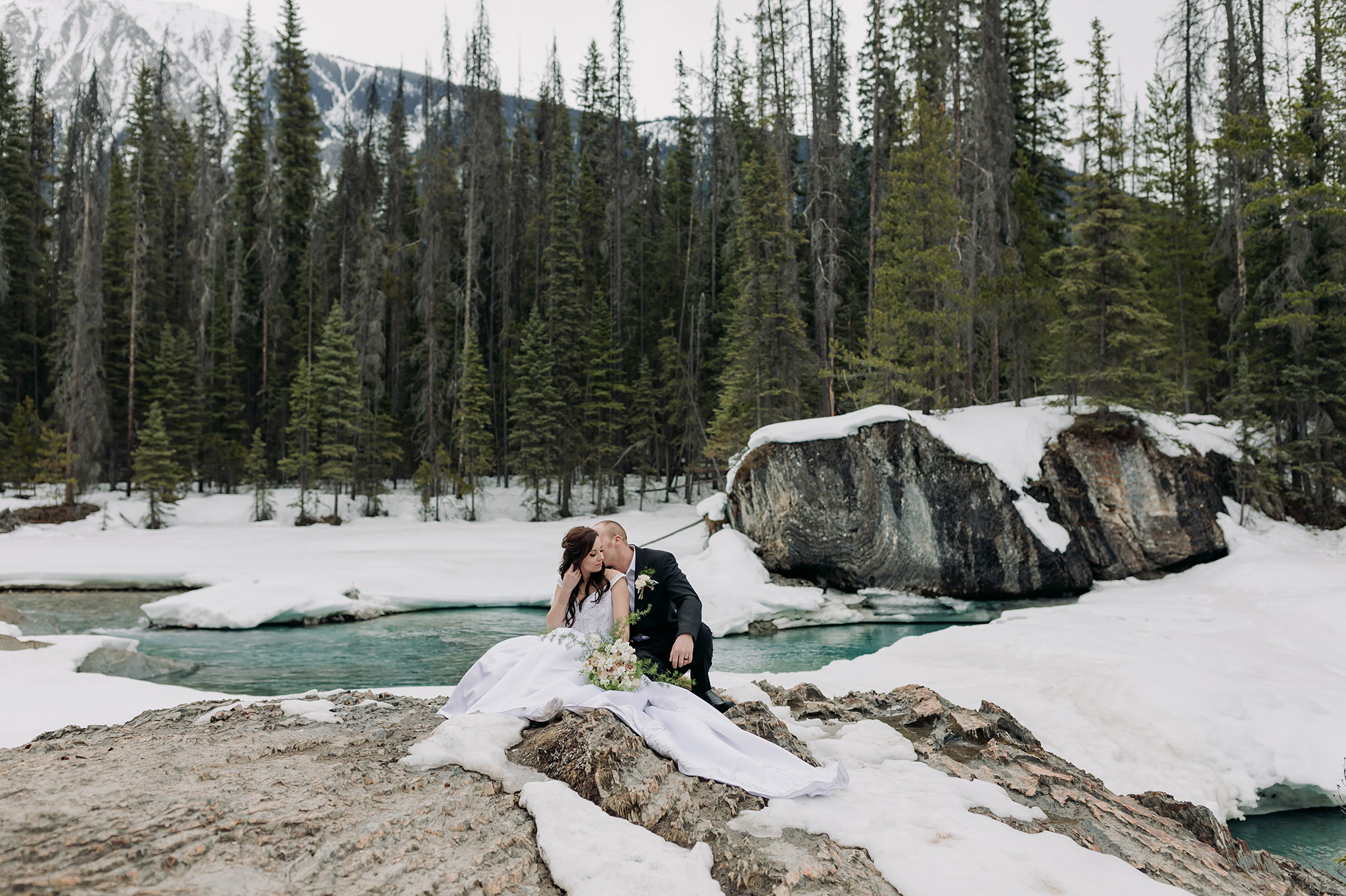 Spring mountain elopement portraits at the natural bridge in yoho national park snow & open river water with incredible blue-green colour