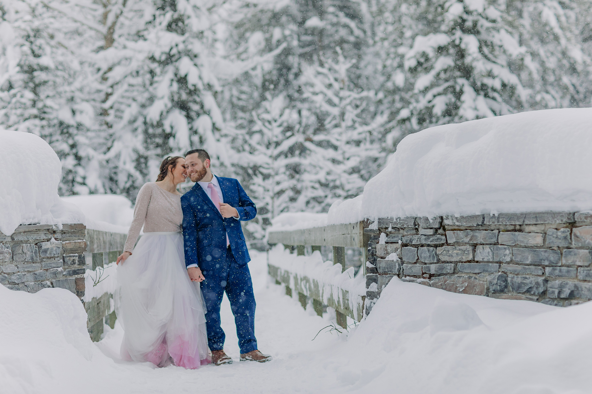Post Hotel wedding portraits on the bridge over the Bow River on super snowy winter day. Bride in rainbow dress.