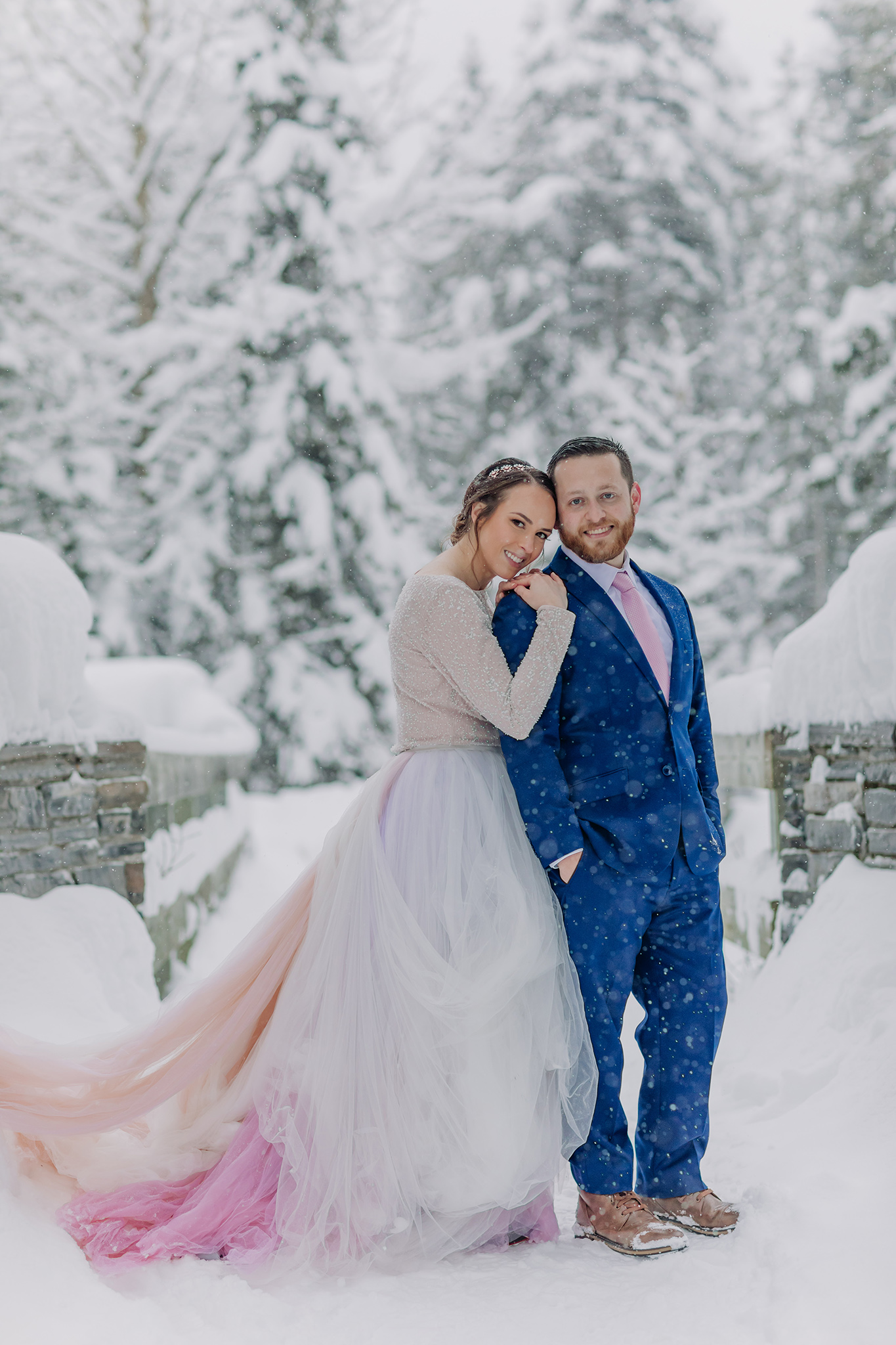 Post Hotel wedding portraits on the bridge over the Bow River on super snowy winter day. Bride in rainbow dress.