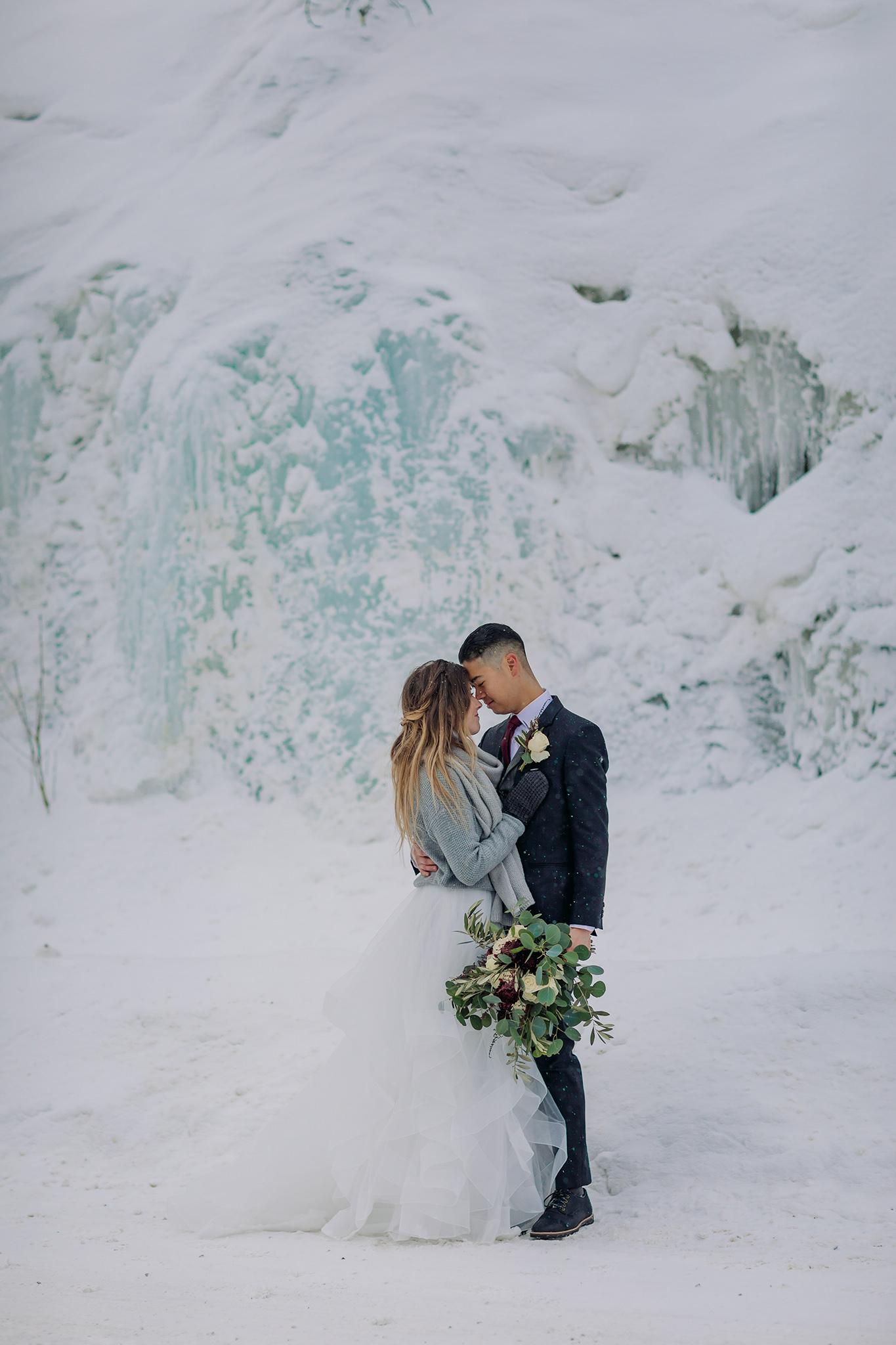 Snowy winter elopement portraits with blue ice near Field, BC in Yoho National Park. Mountain wedding in a winter wonderland. Bride in a cozy sweater & matching scarf to keep warm. What to wear for a winter wedding. 