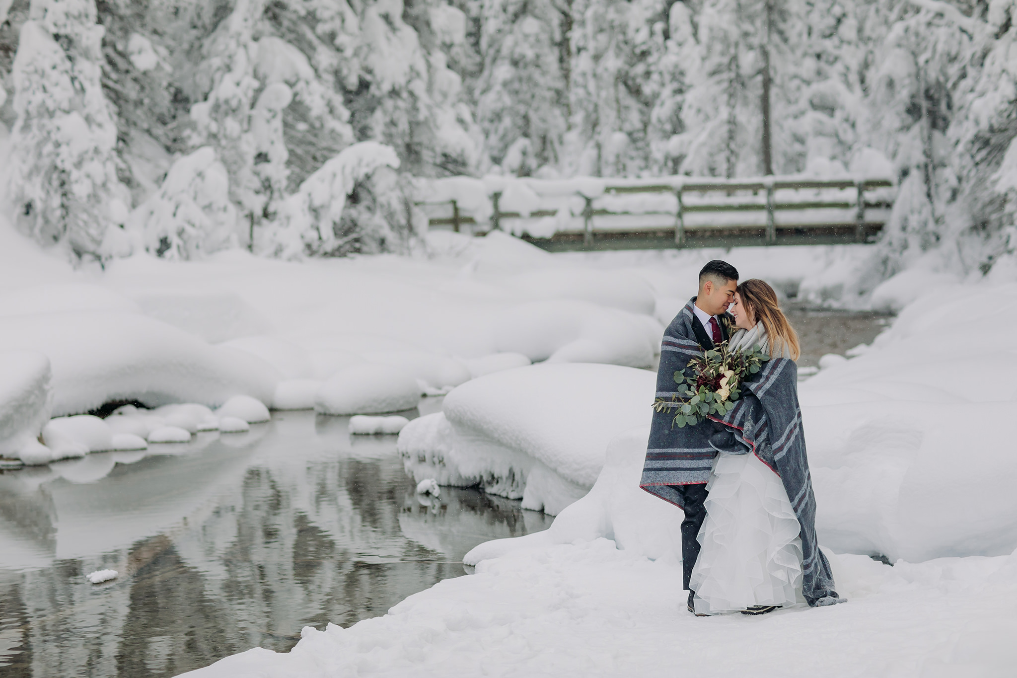 wedding portraits at Emerald Lake Lodge in Yoho National Park. Mountain wedding in a winter wonderland. Newlyweds cuddled in grey plaid blanket. 