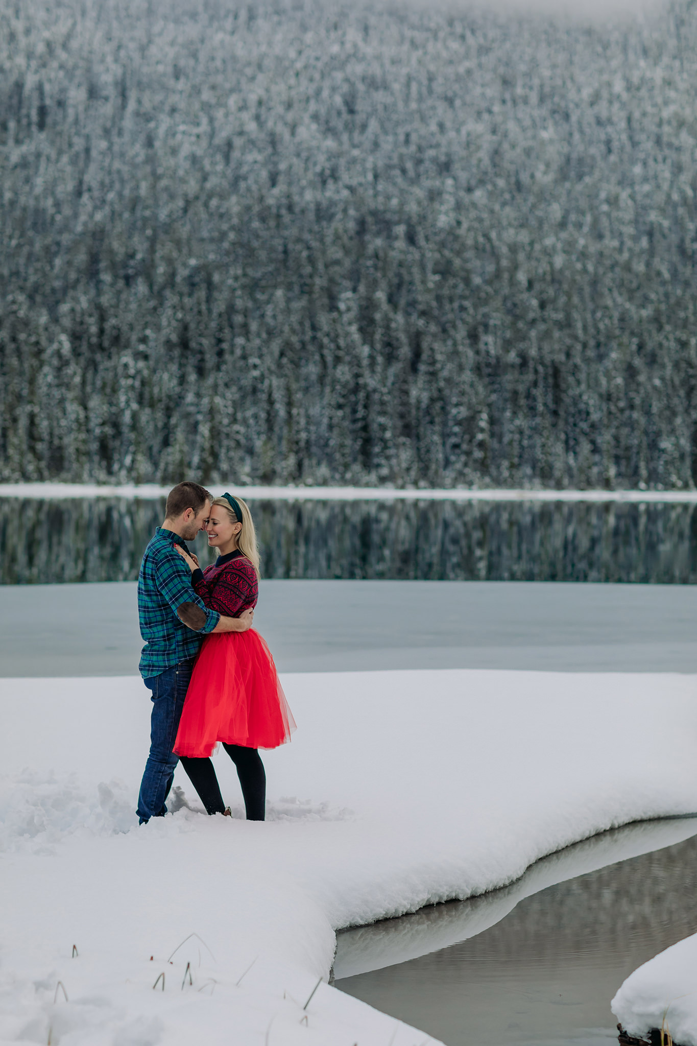 emerald lake winter engagement photos with freshly frozen lake featuring playful red tulle skirt & nordic sweater