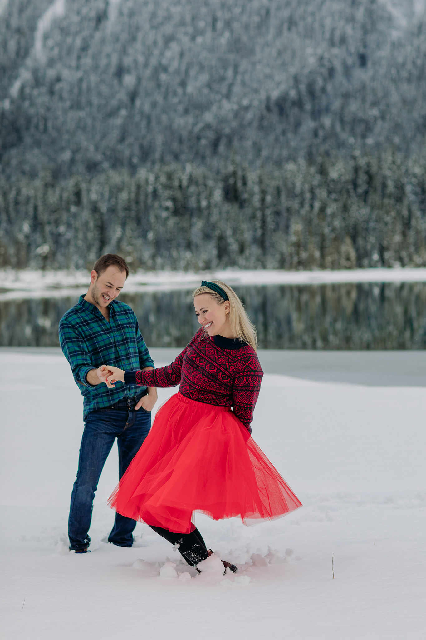 emerald lake winter engagement photos with freshly frozen lake featuring playful red tulle skirt & nordic sweater