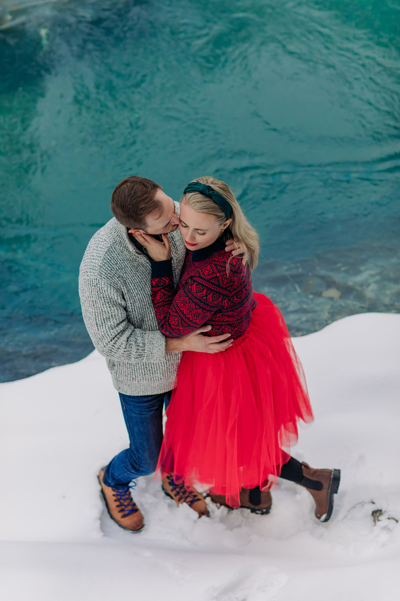 snowy natural bridge couples photos with freshly frozen lake featuring playful red tulle skirt & nordic sweater
