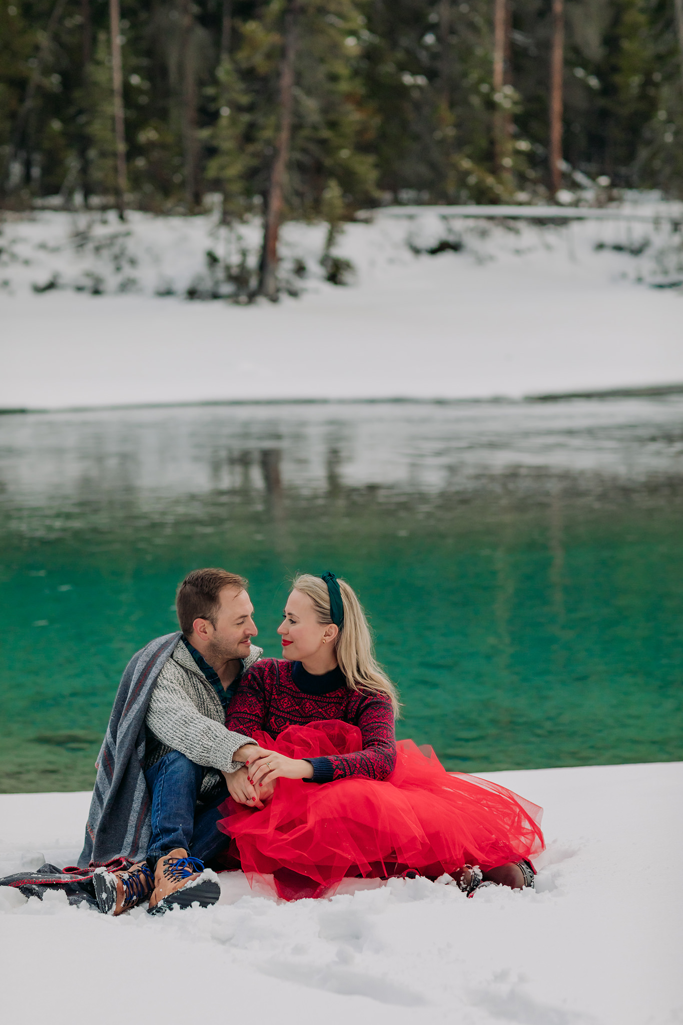 snowy natural bridge couples photos with freshly frozen lake featuring playful red tulle skirt & nordic sweater