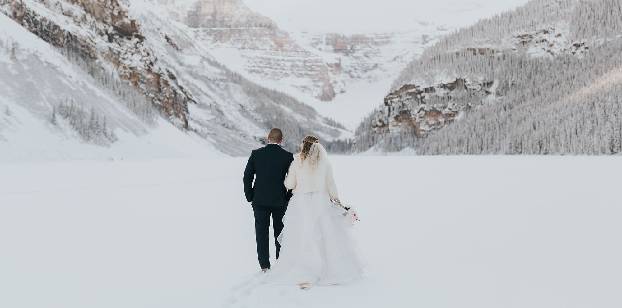 newly wed bride & groom walking on frozen Lake Louise in December