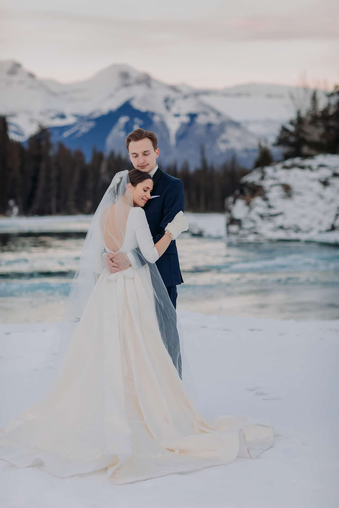 newlyweds cuddling on frozen Bow River at Bow Falls in Banff National Park for their winter wedding portraits
