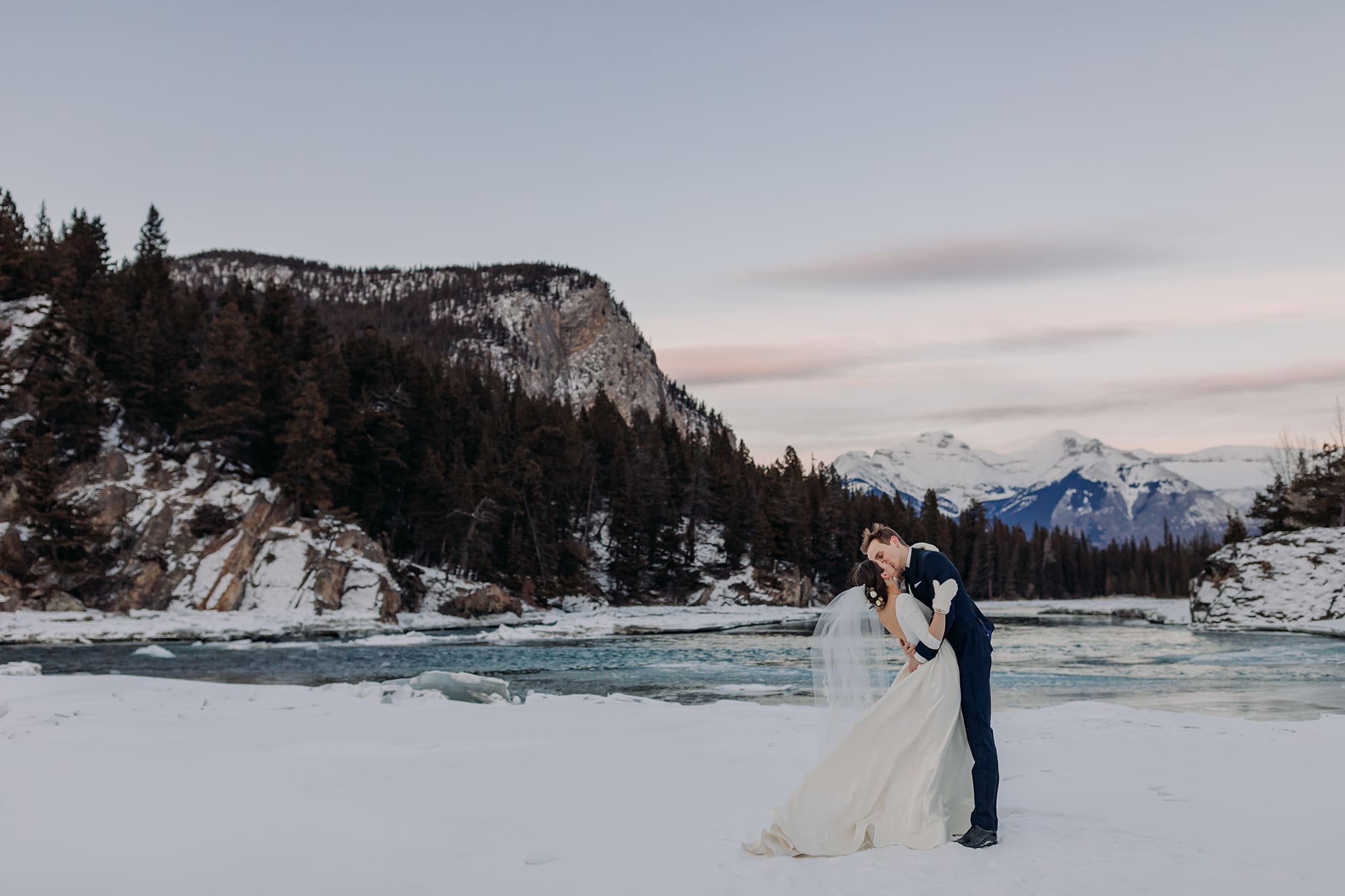 dramatic winter sunset kiss on the Bow River near Bow Falls in Banff National park winter wedding