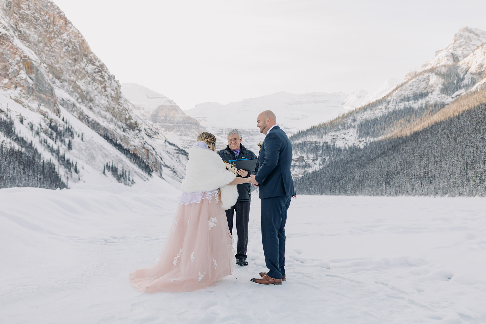 Lake Louise winter elopement ceremony on the frozen Lake Bride in pink wedding dress in winter wonderland Super snowy wedding ceremony photographed by ENV Photography