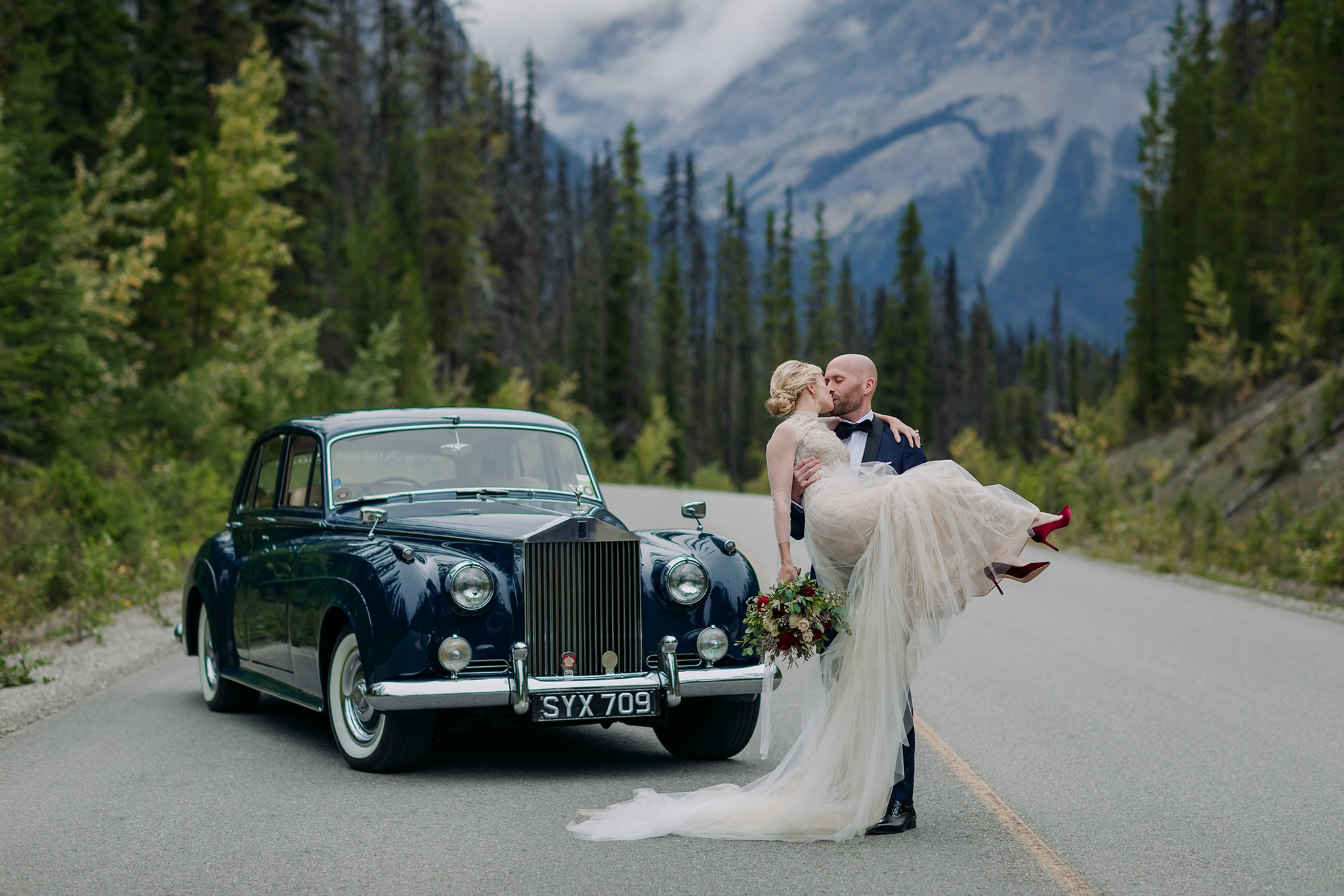 A Guide to Eloping in the Canadian Rockies | Mountain Wedding photographed by ENV Photography | Elegant mountain elopement. Bride in Vera Wang swept off her feet on the road to Emerald Lake Lodge. Vintage Rolls Royce wedding car.