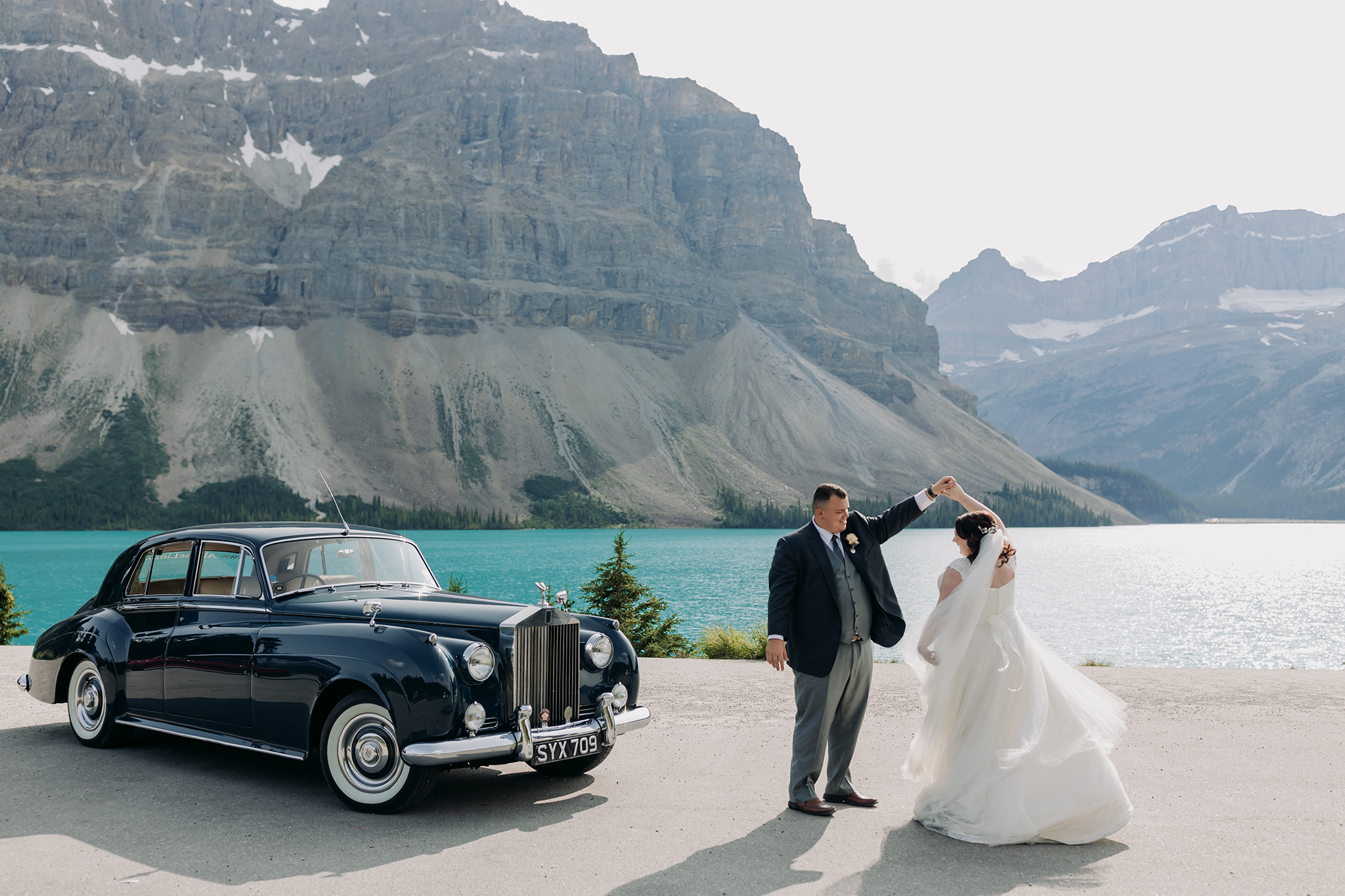 A Guide to Eloping in the Canadian Rockies | Mountain Wedding photographed by ENV Photography | bride & groom dancing in the road at bow lake on icefields parkway in with Rolls Royce